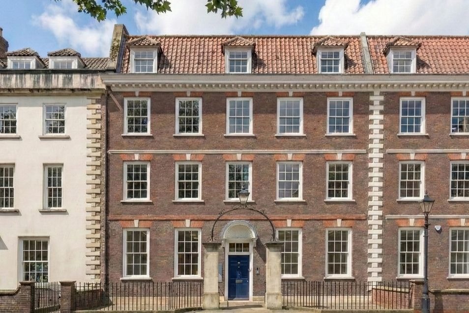 Georgian-style brick building with symmetrical white-framed windows, dormers, and a navy blue front door under an arched lamp.