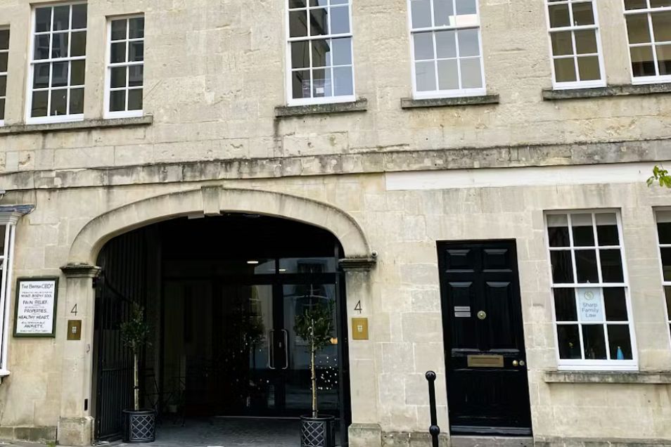 Historic stone building facade featuring a large arched entryway, white-framed sash windows, and a black front door with gold hardware.