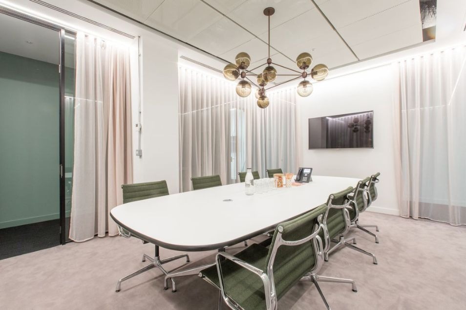Conference room featuring an oval white table, green ribbed leather chairs, and a gold chandelier.