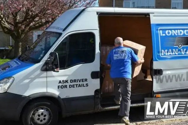 A mover in a blue uniform loads a large cardboard box into the side door of a white and blue London Man Van.