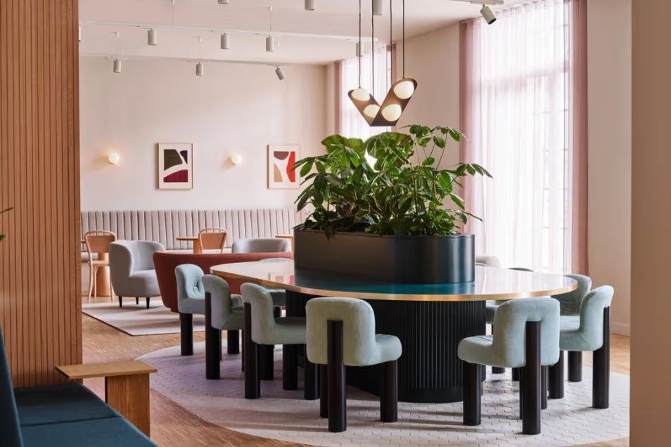 Lounge features a large circular table with a central plant and soft blue curved chairs.