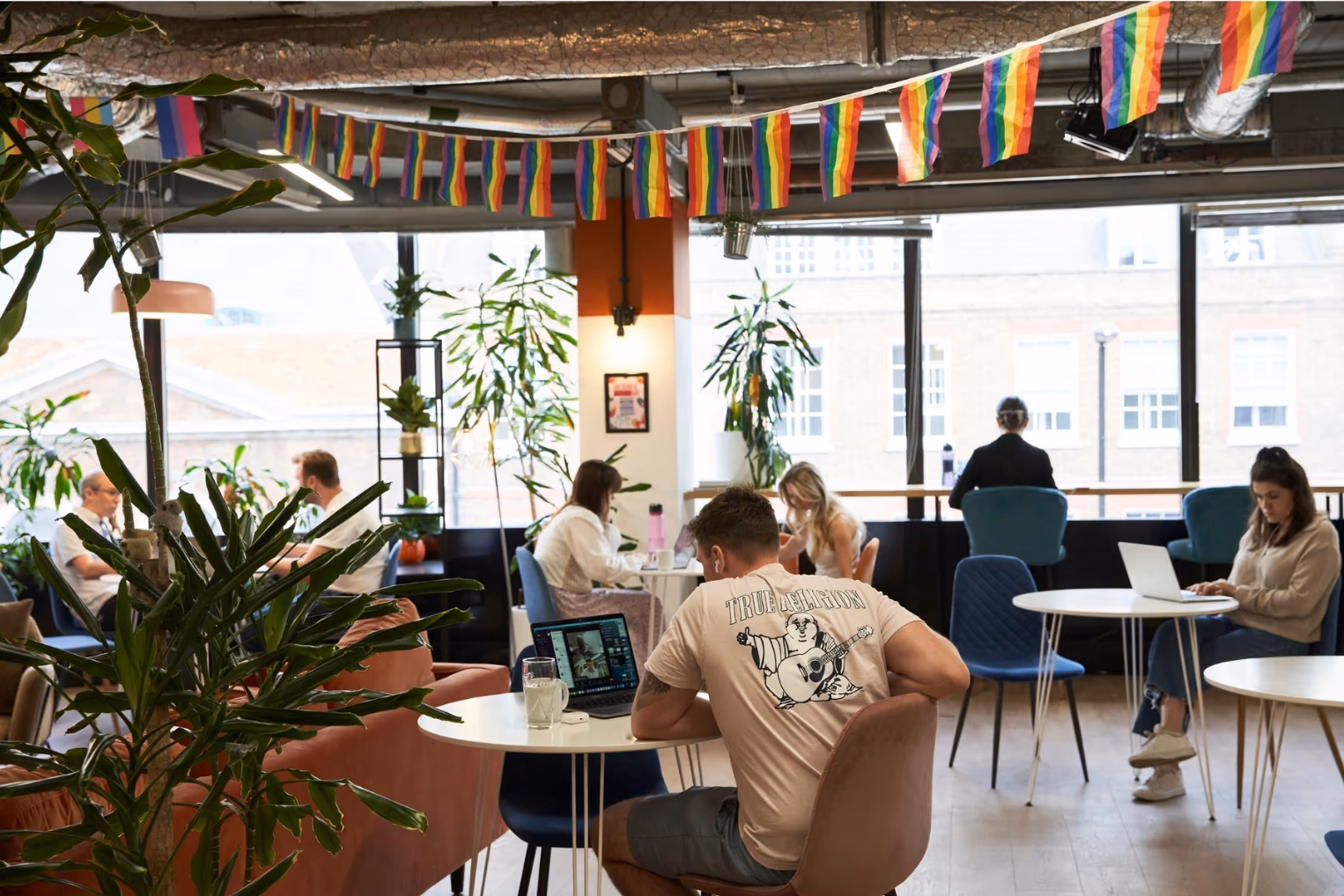 coworking lounge with an orange velvet sofa, a blue armchair, and a black geometric shelf filled with plants and decor.