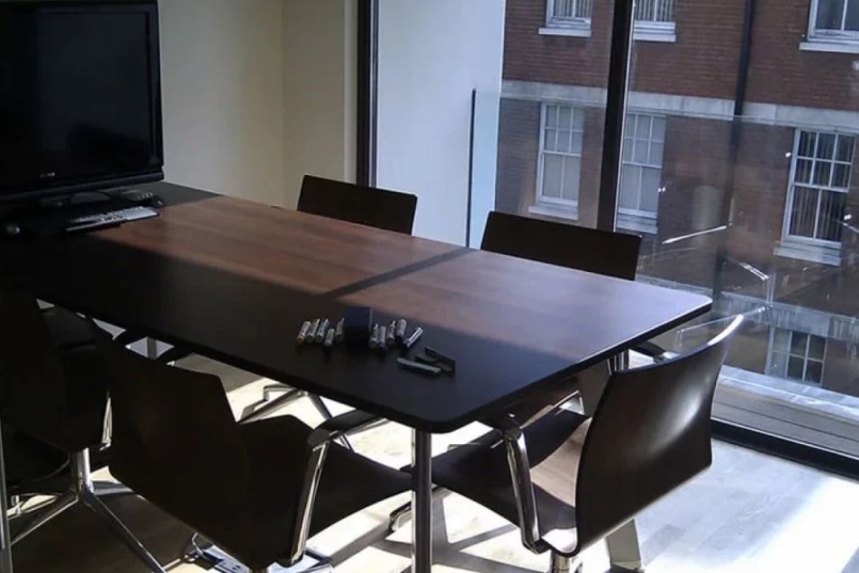A dark-topped conference table with black chairs situated next to a large window overlooking city buildings.