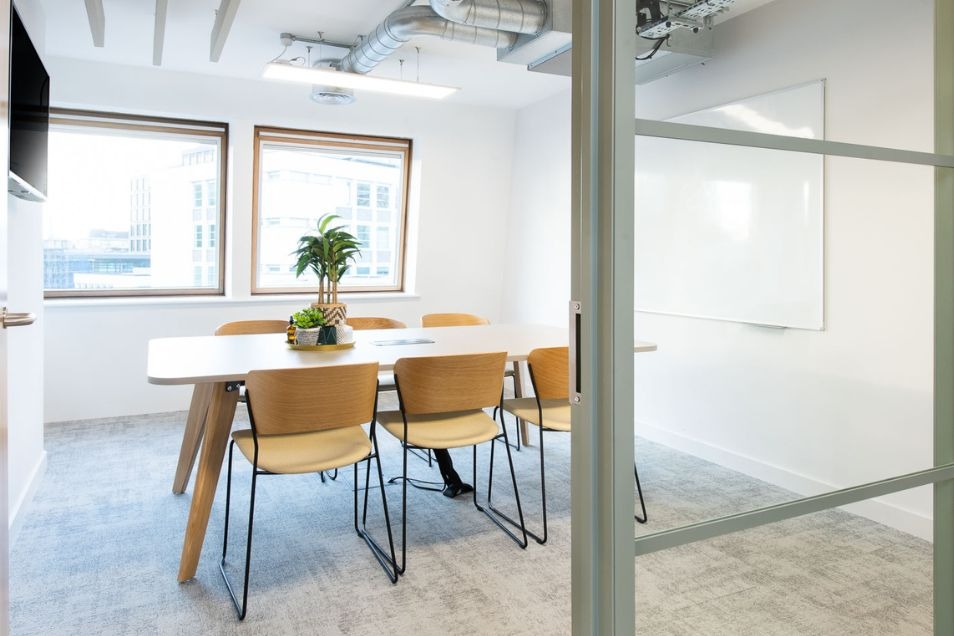 Minimalist meeting room viewed through a glass  door, featuring a light wood table and matching chairs.