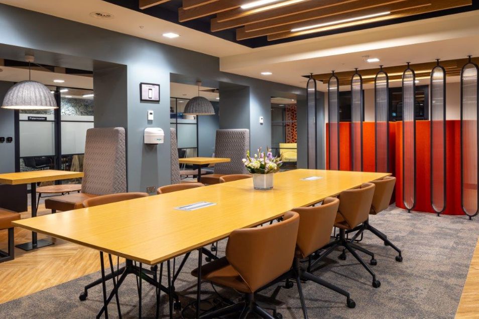 Meeting room with a long yellow table, tan leather chairs, and a decorative orange room divider.