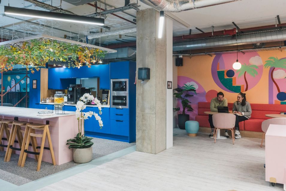 Two people sit and work at a small table in a vibrant kitchen area with blue cabinetry.