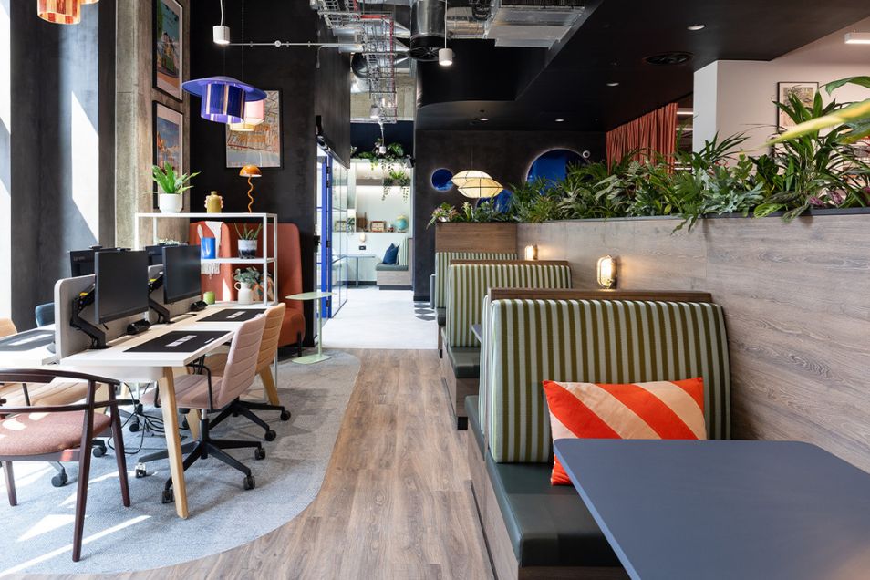 An office featuring striped privacy booths with orange pillows alongside a row of white computer workstations.