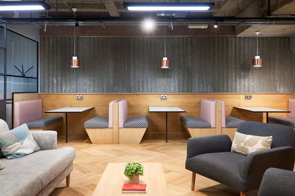 An office break area with booth seating, small tables, and armchairs on a herringbone pattern floor.