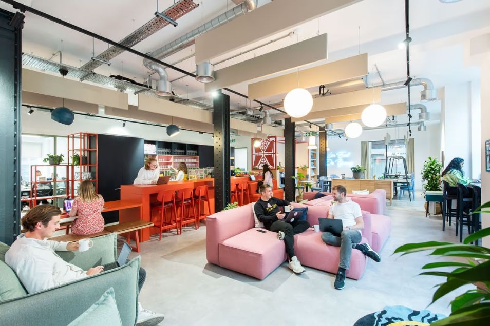 People sat on pink sofas and at an orange bar working on laptops in an open office lounge.
