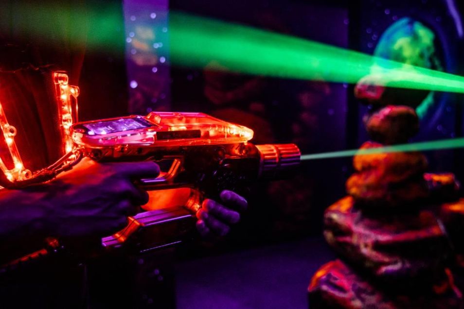 A hand holds a laser tag gun that emits a beam of light in a dark room.