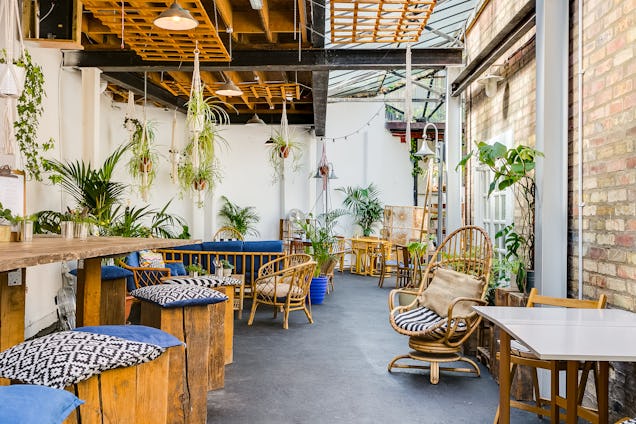 Chairs and tables are arranged in an indoor patio area with brick walls and hanging plants.