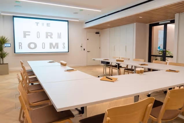 Modern u-shaped conference table with wooden chairs and a large projection screen displaying "THE FORM ROOMS."