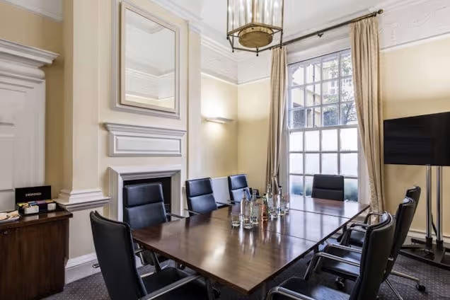 boardroom with a dark wood table, black leather chairs, a traditional fireplace, and large sash windows.