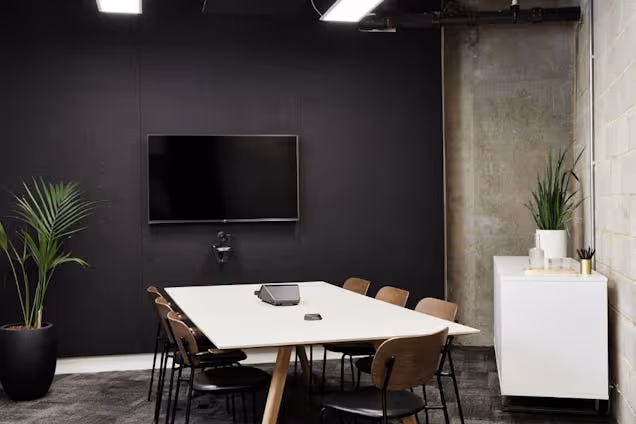 Meeting room with a white table, dark wood chairs, a black feature wall, and an exposed concrete pillar.