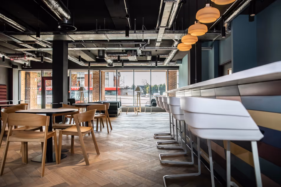 Office cafe with herringbone wood floors, wooden dining sets, white bar stools, and industrial exposed ductwork.