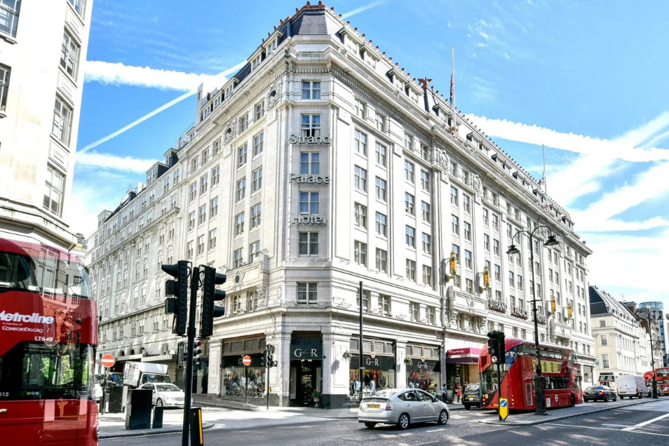 Grand white stone corner building in London, featuring classical architecture and red double-decker buses on the street below.