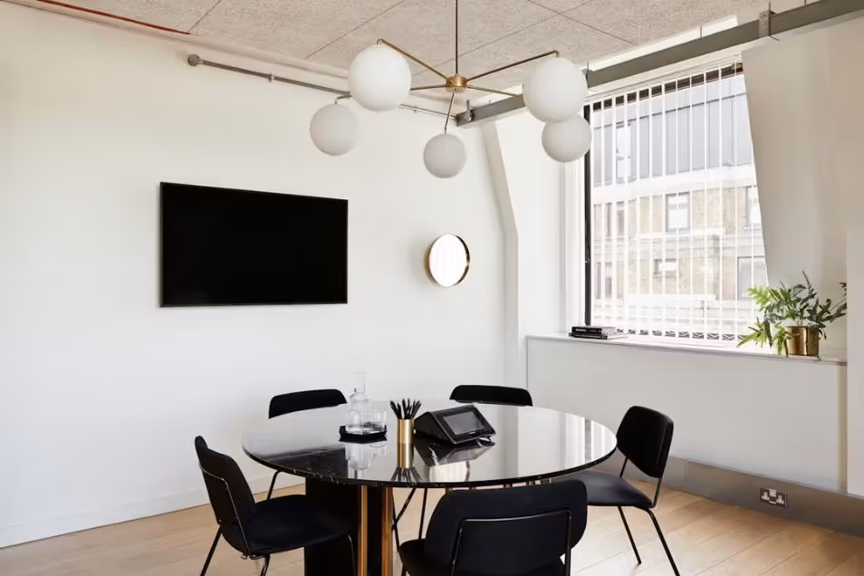 Meeting room with a round black table, matching chairs, a large globe chandelier, and a wall-mounted flat screen.