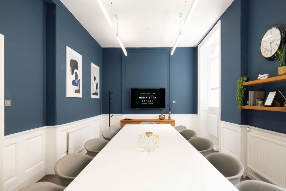 Meeting room with a long white table, grey chairs, slate blue walls, and white wainscoting.