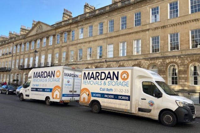 Two white and orange Mardan Removals & Storage vans parked on a street in front of a stone terrace building.