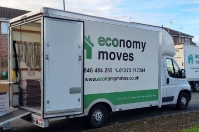 A white Economy Moves truck with a green logo and an open back door showing straps inside.