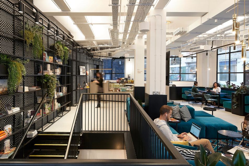 People sitting at desks in a multi-level office space with a metal staircase and indoor plants.