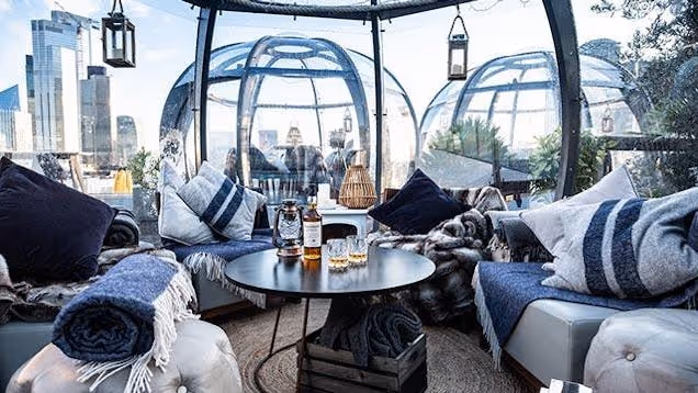 Seating areas inside glass igloos on a rooftop terrace overlooking a city skyline.