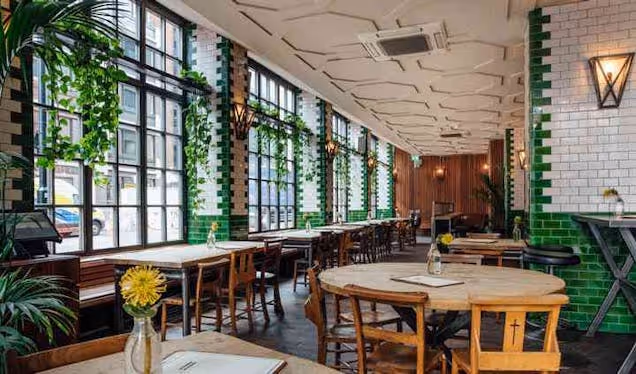 Tables and chairs inside the Singer Tavern bar featuring tiled walls and windows with plants.