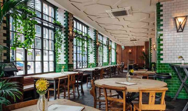 Tables and chairs inside the Singer Tavern bar featuring tiled walls and windows with plants.