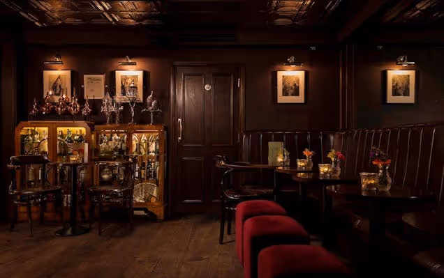 A bar interior with wooden paneling, red stools, and framed pictures on the wall.