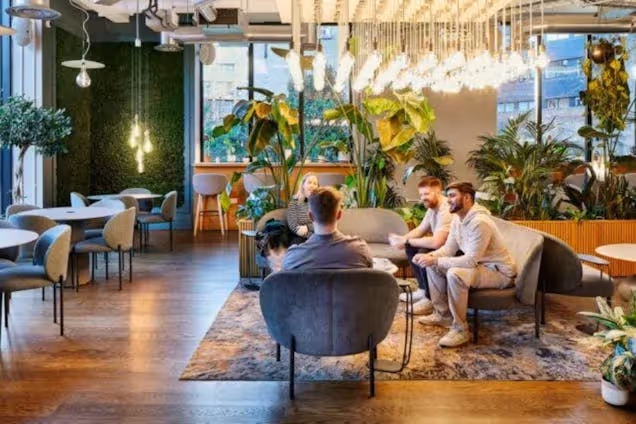 People sitting in chairs and on sofas in a coworking space with indoor trees and plants under wood-panelled ceilings.