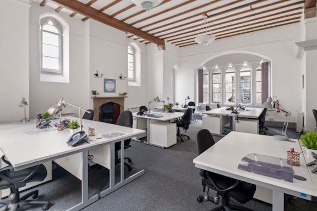 An office with white desks and black chairs in a room featuring arched windows and wood ceiling beams.