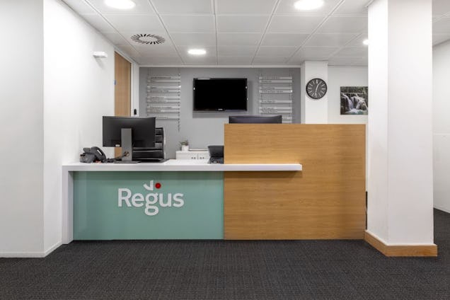 A reception desk with a Regus logo and a computer monitor in an office reception area with white walls.