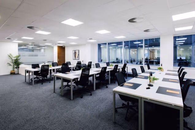 An office featuring rows of white desks and black chairs in front of glass partitions.