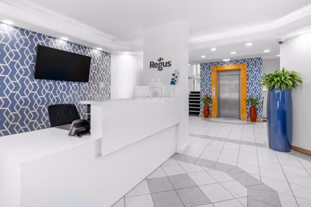 A white reception desk stands in a lobby with patterned blue walls and an elevator.