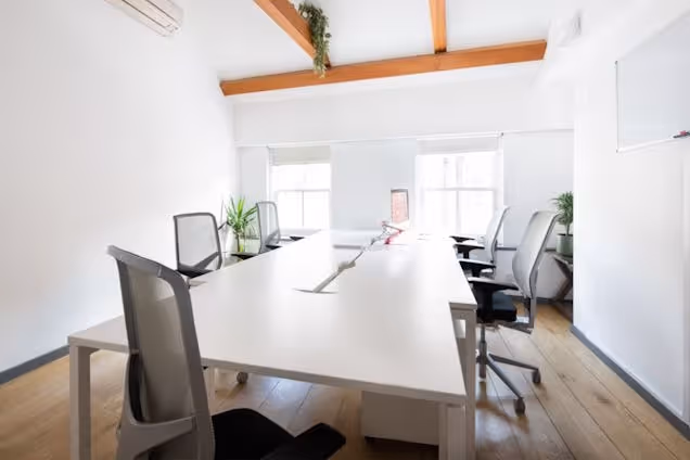 White desks and grey chairs are in an office with wood floors and exposed ceiling beams.
