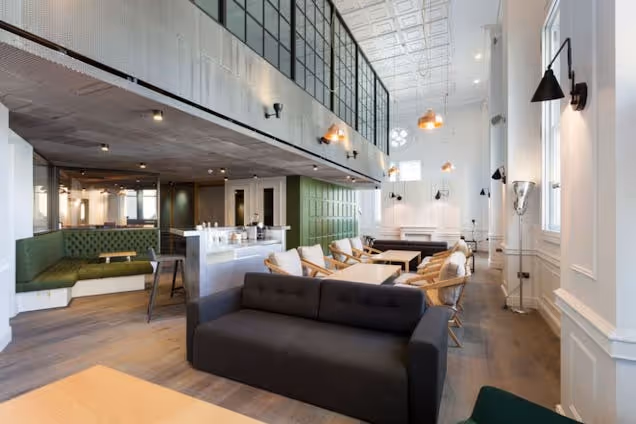 A lounge area with a black sofa and wooden chairs next to a bar counter and booth seating in an office.