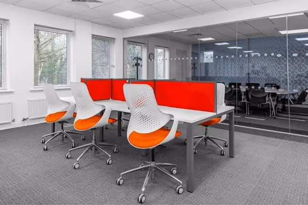 Orange and white chairs at white desks with red partitions in a coworking space.