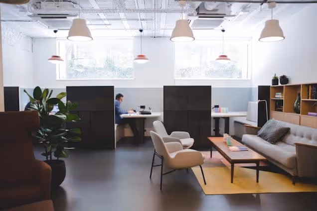 A person works at a desk next to a lounge area with a sofa, chairs, and table.