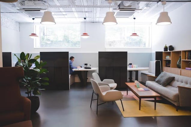 A person works at a desk next to a lounge area with a sofa, chairs, and table.