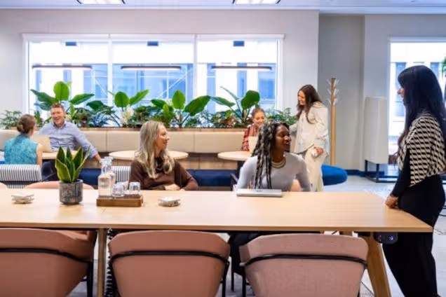 People sat talking around a wooden table in a coworking space with chairs and plants.