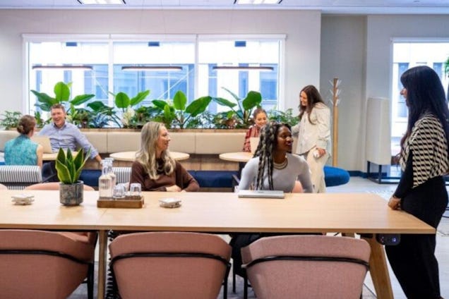 People sat talking around a wooden table in a coworking space with chairs and plants.