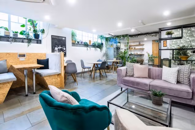 Velvet sofas and armchairs near wooden booths and tables in a lounge area with indoor plants.