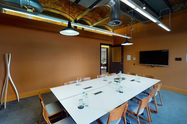 A white table with chairs in a meeting room with tan walls, blue carpet, and pendant lights.