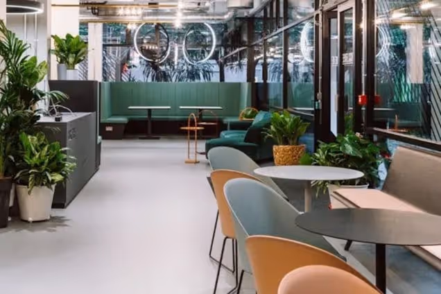 Green booths and tables with chairs in a coworking area with plants and large windows.
