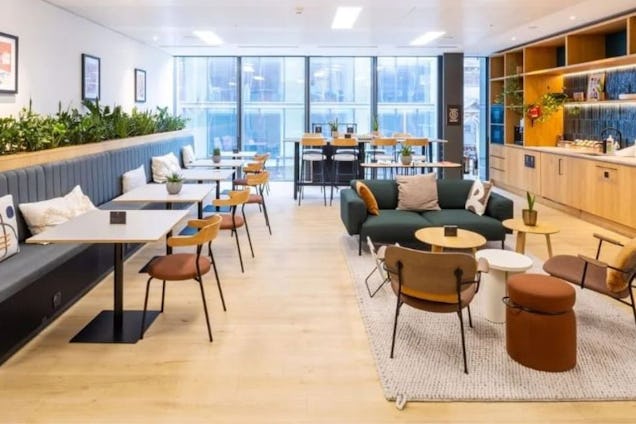 Chairs and tables sit near a built-in bench and a lounge area with a sofa in an office breakout space.