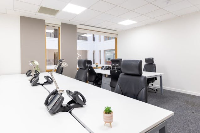 Desk phones on white desks with black chairs in an office with grey carpeted floors.