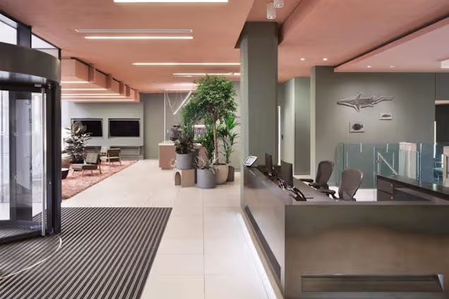 A reception desk in a reception area with a revolving door and plants in the background.