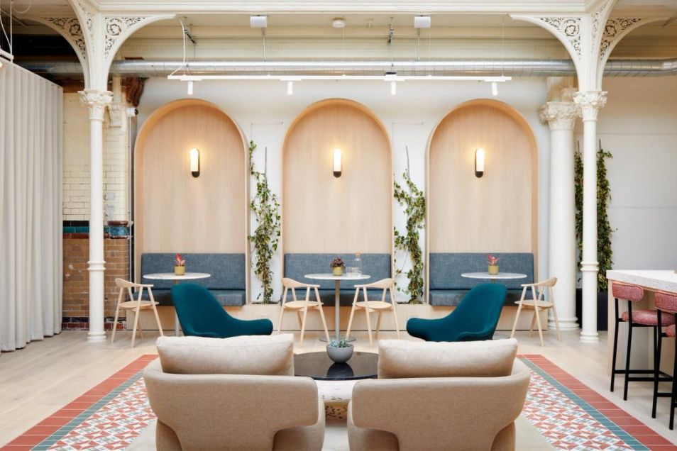 Cream and teal armchairs and small tables are arranged in a coworking space with arches and wooden wall panels.
