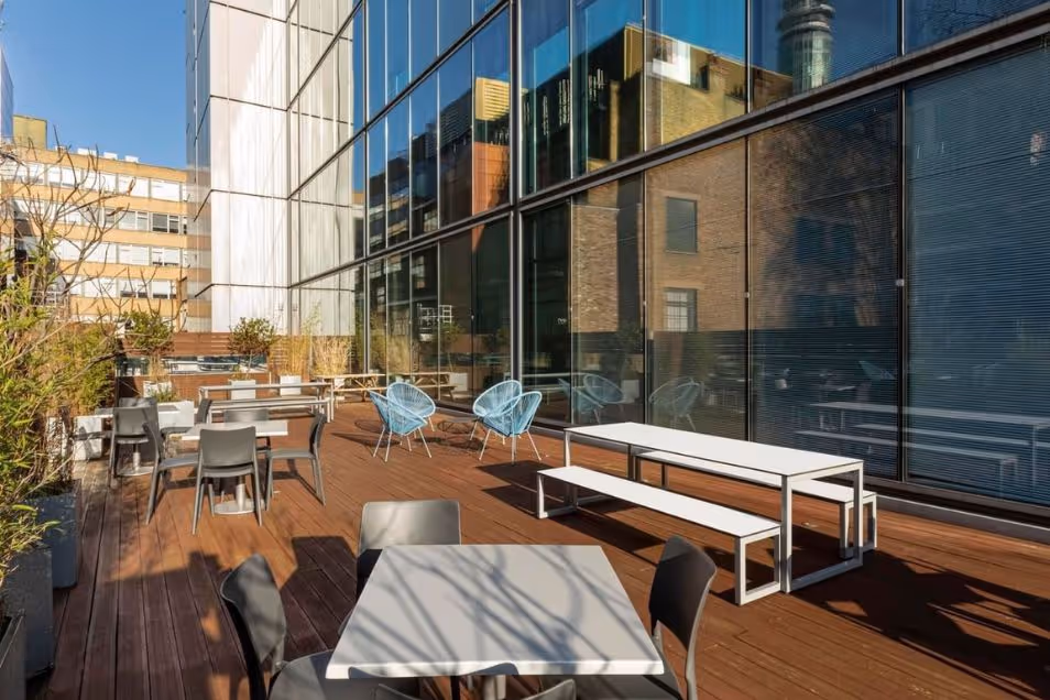 Tables and chairs on a wooden roof terrace next to a glass building.