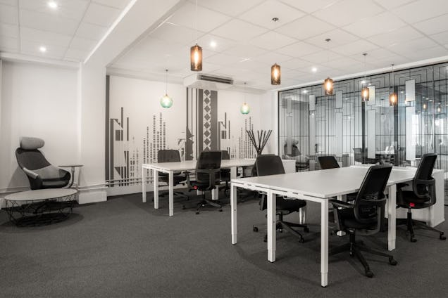Black chairs and white desks sit in an office with carpet, an armchair, and pendant lights.